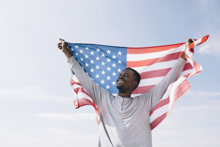 Smiling man holding U.S. flag, symbolizing success in the I-485 Application process.